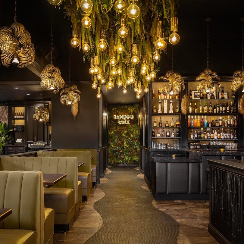 Interior of Bamboo Walk Caribbean Restaurant with olive green booths, a full bar, and tropical decor.