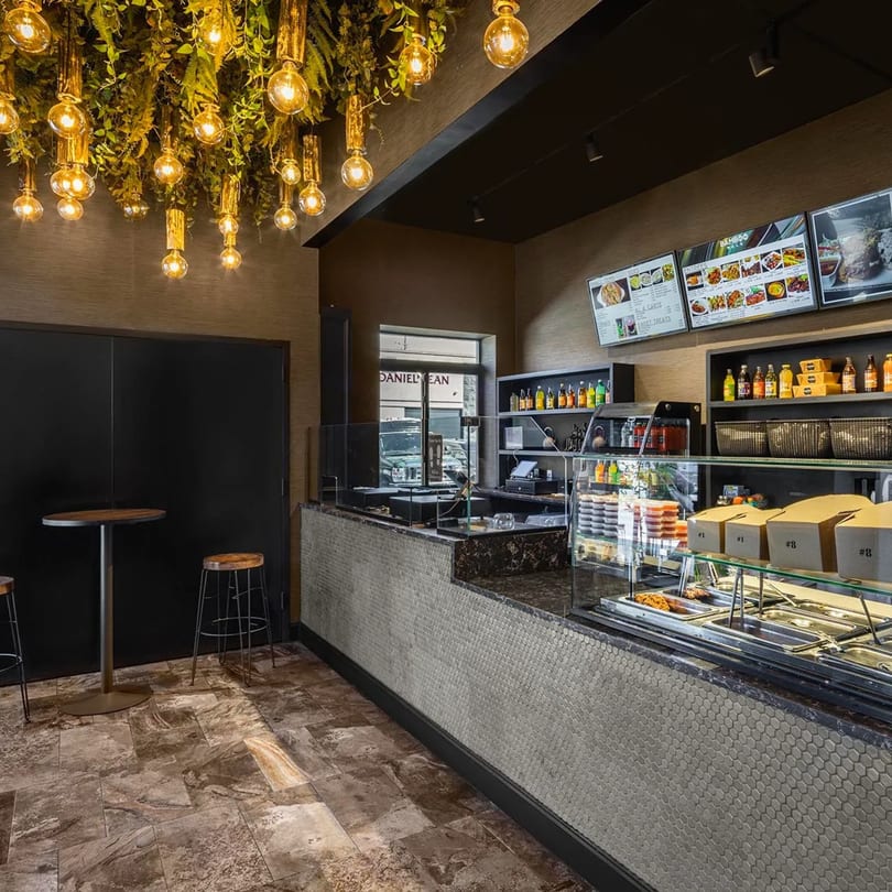 Interior of Bamboo Walk Caribbean Restaurant with a counter, menu screens, and decorative hanging lights.