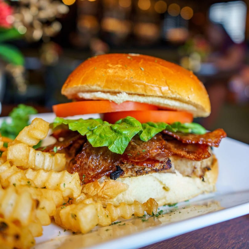 A Caribbean jerk chicken sandwich with lettuce, tomato, and bacon, served with crinkle-cut fries.