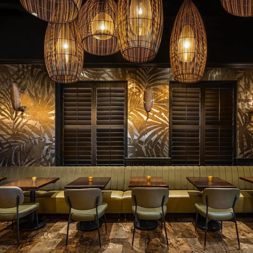 Bamboo Walk Caribbean Restaurant interior with bamboo light fixtures, tropical wallpaper, and olive green seating.