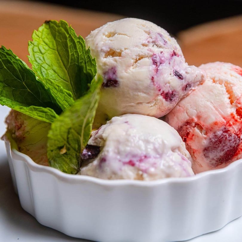 Scoops of berry-swirled ice cream with fresh mint leaves in a white bowl.