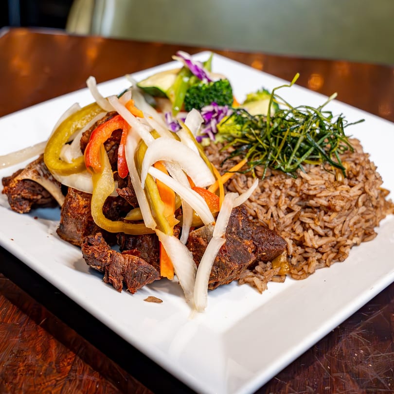 Caribbean fried chicken with rice, pickled vegetables, and a side salad on a white plate.