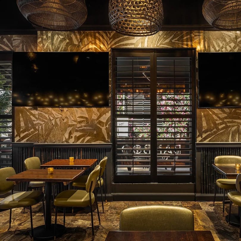 Bamboo Walk Caribbean Restaurant interior with dark wood tables, green chairs, and tropical leaf wallpaper.